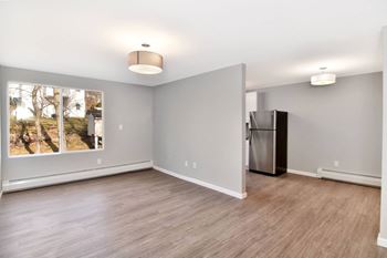 An empty living room with a large window and a refrigerator
